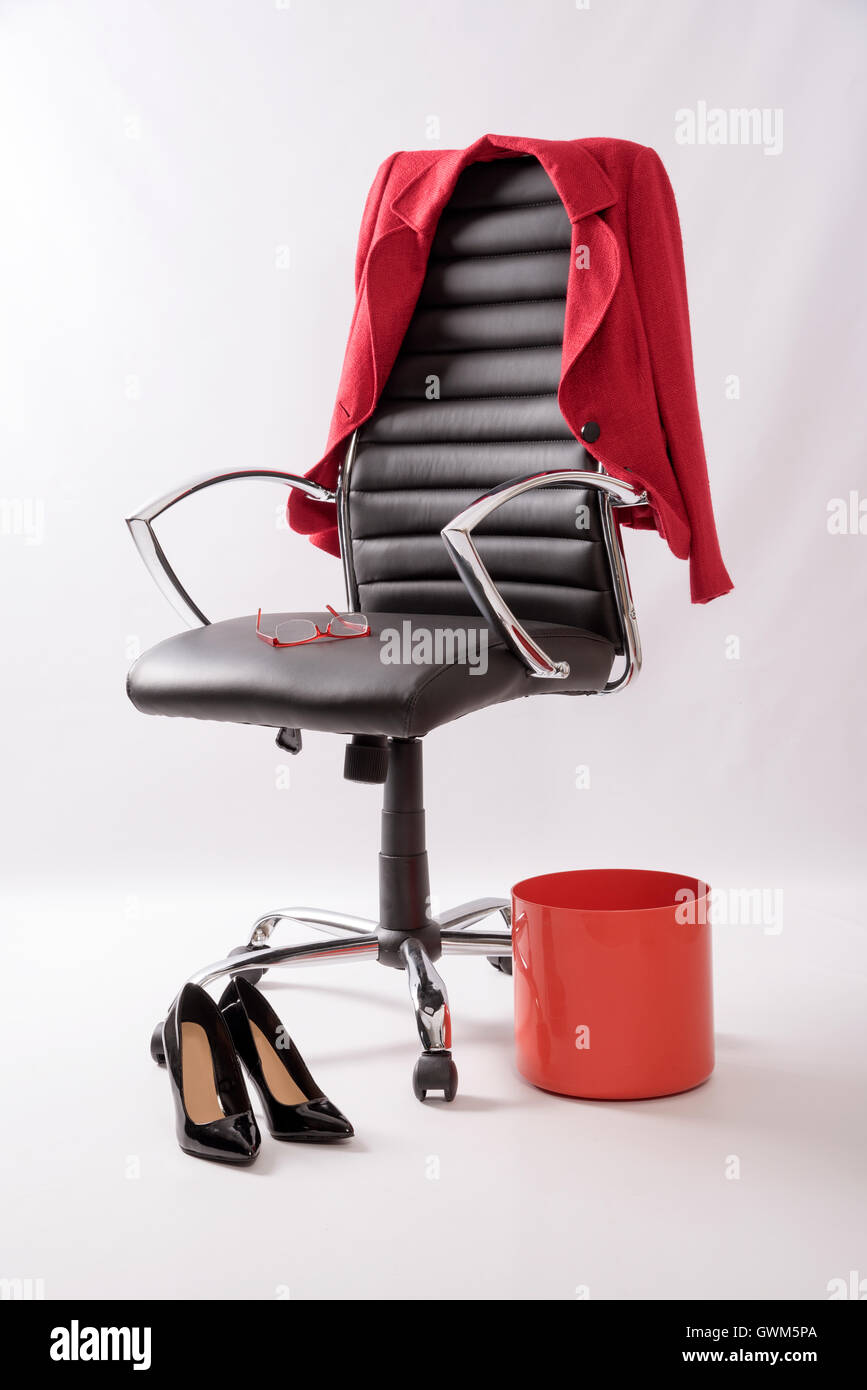 Un fauteuil en cuir noir avec un manteau rouge poubelle, hautes chaussures de talon et une paire de lunettes sur le siège Banque D'Images