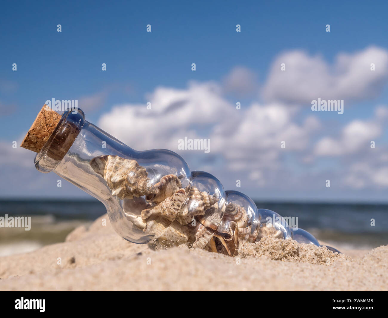 Bouteille bouchonnée avec coquillages coincé dans le sable sur la plage Banque D'Images