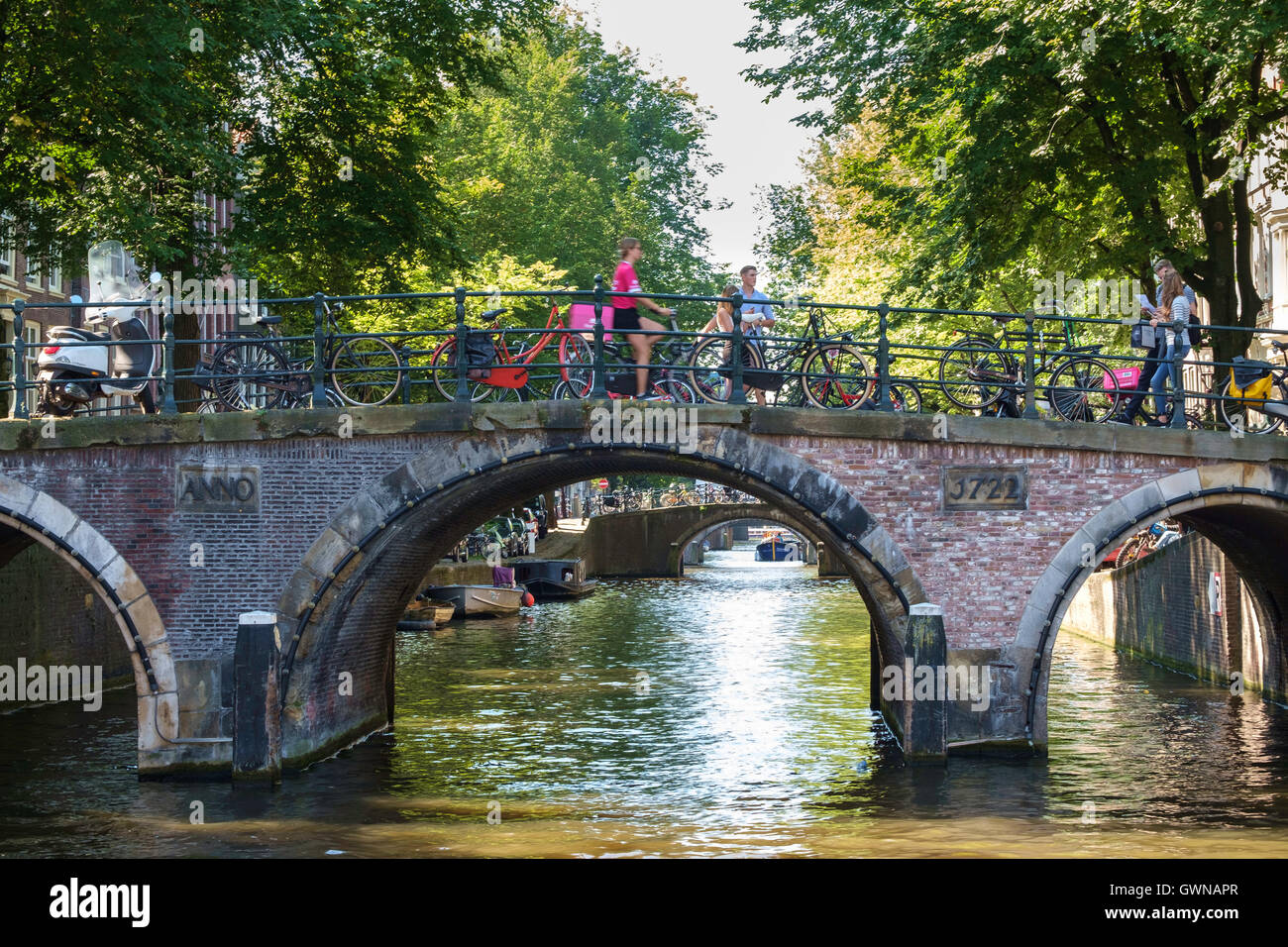 Les cyclistes et les touristes traversent un pont-canal ensoleillée à Amsterdam. Banque D'Images