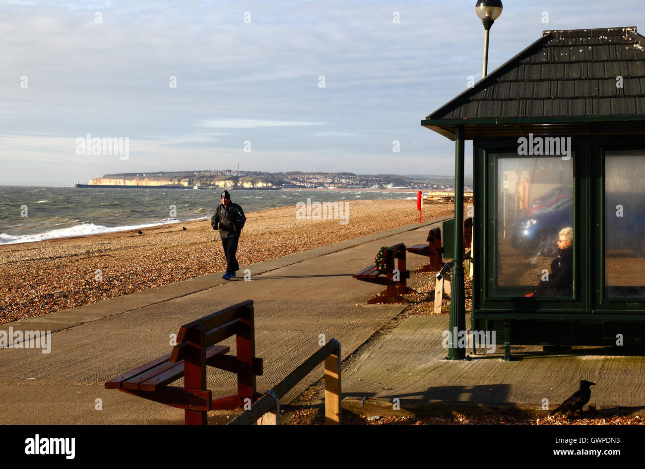 Vieille dame assise dans un abri sur le front de mer sur un après-midi d'hiver, Newhaven en arrière-plan, Jalhay, East Sussex, Angleterre Banque D'Images