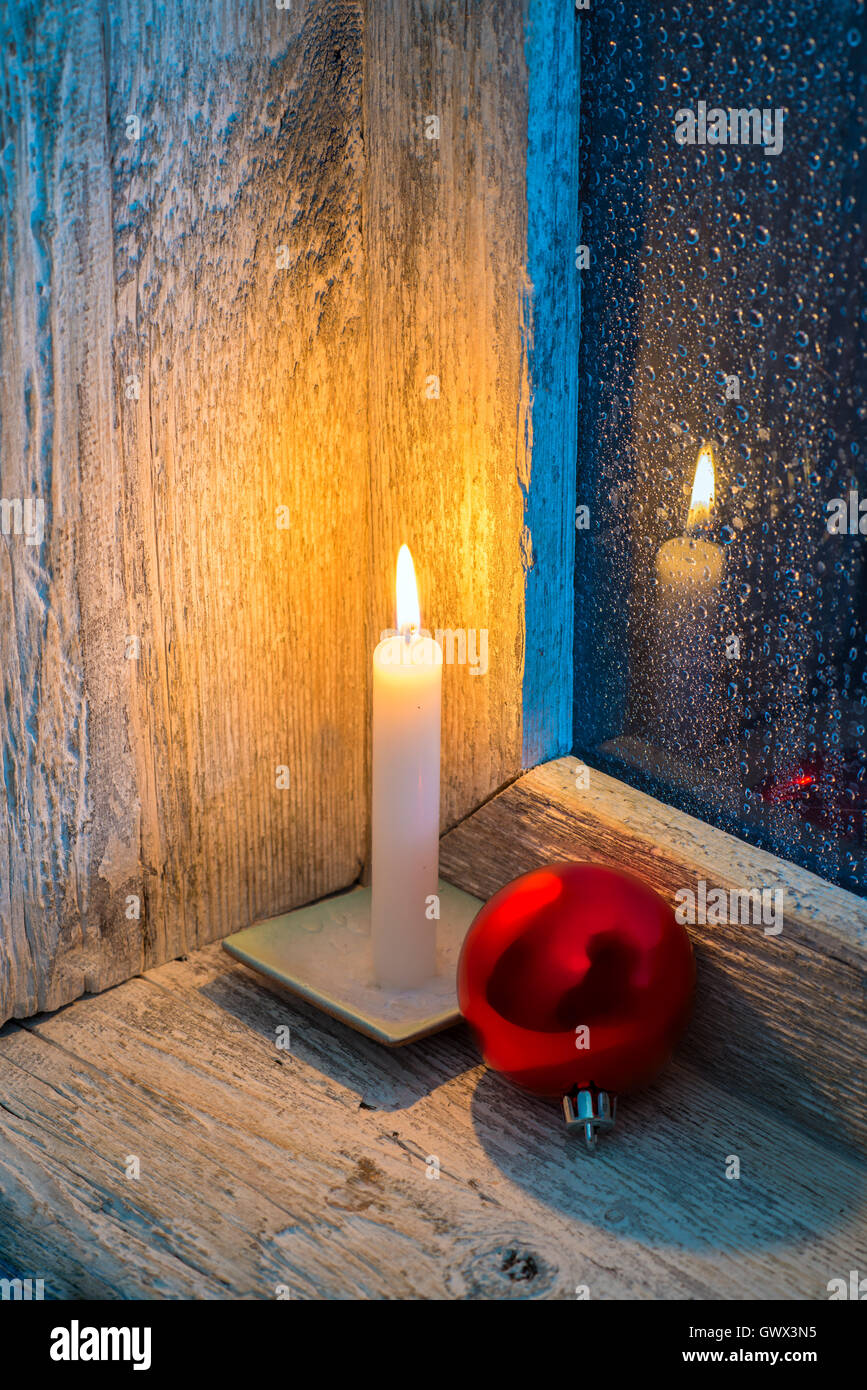 Bougie brûlante et ornements de Noël dans une ancienne fenêtre avec verre humide Banque D'Images