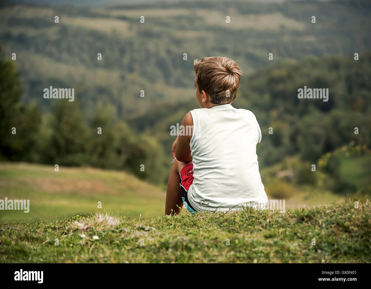 Garçon assis sur une colline et regarde au loin. L'enfance, les rêves, la liberté - un concept. Banque D'Images