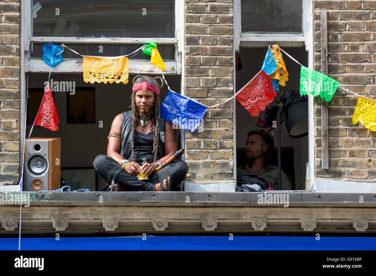 Les gens sous windows pendant le 50e carnaval de Notting Hill ; fenêtres décorées de guirlandes colorées Banque D'Images