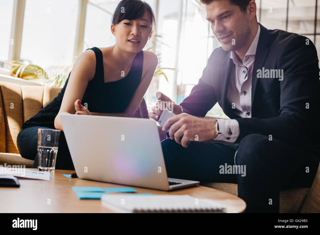 Shot of young woman sitting in lobby et travaillant sur un ordinateur portable. Businessman and businesswoman discussion de nouvelles proje Banque D'Images
