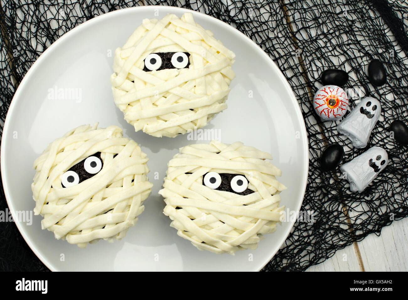 Groupe d'Halloween cupcakes maman sur plaque blanche avec bonbons sur fond de tissu noir Banque D'Images
