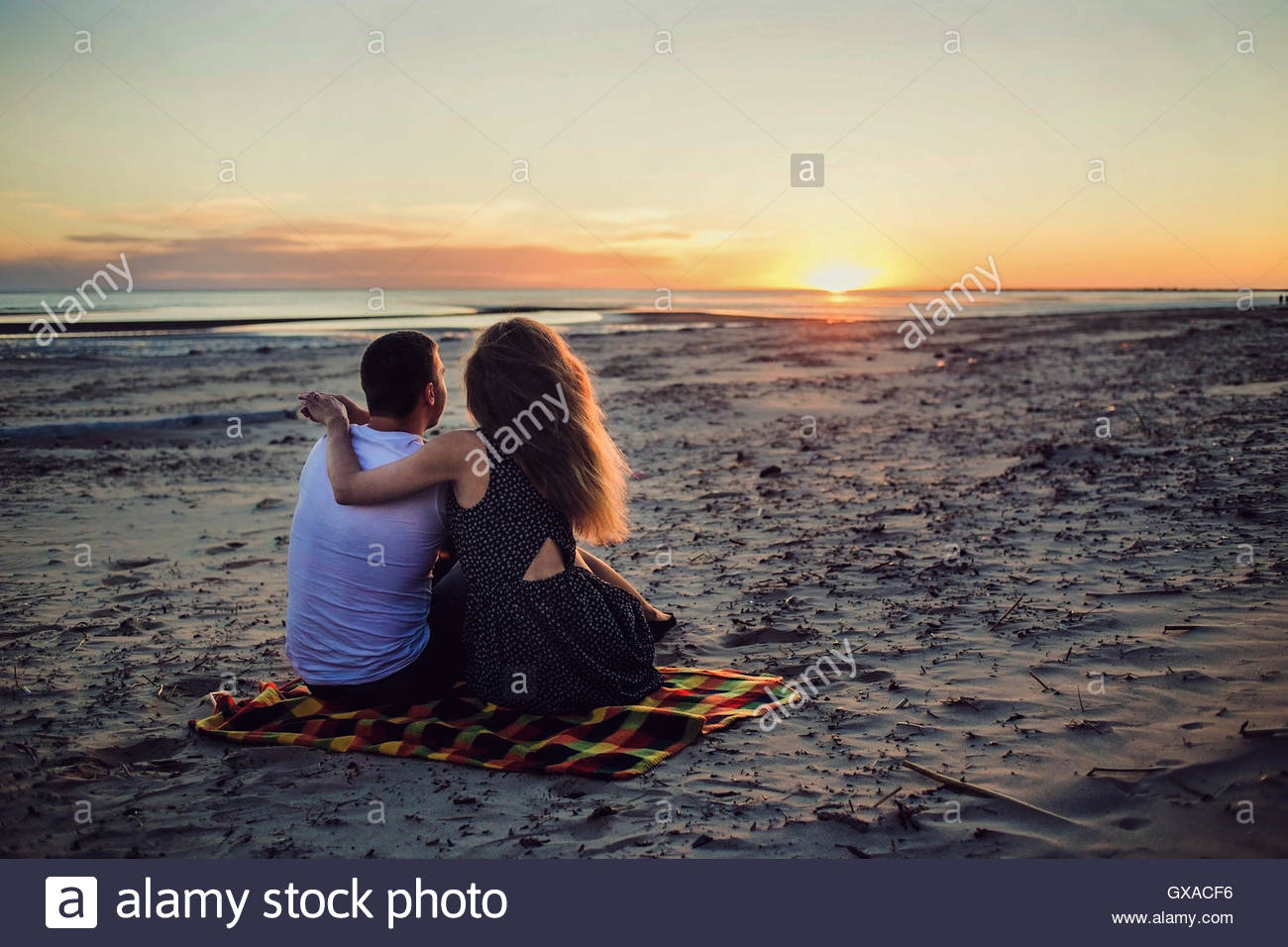 Couple Assis Près De La Mer Sur Le Coucher Du Soleil Banque