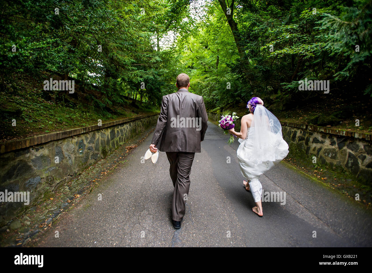 Couple nouvellement marié passe la forêt Street en direction de l'objectif Banque D'Images