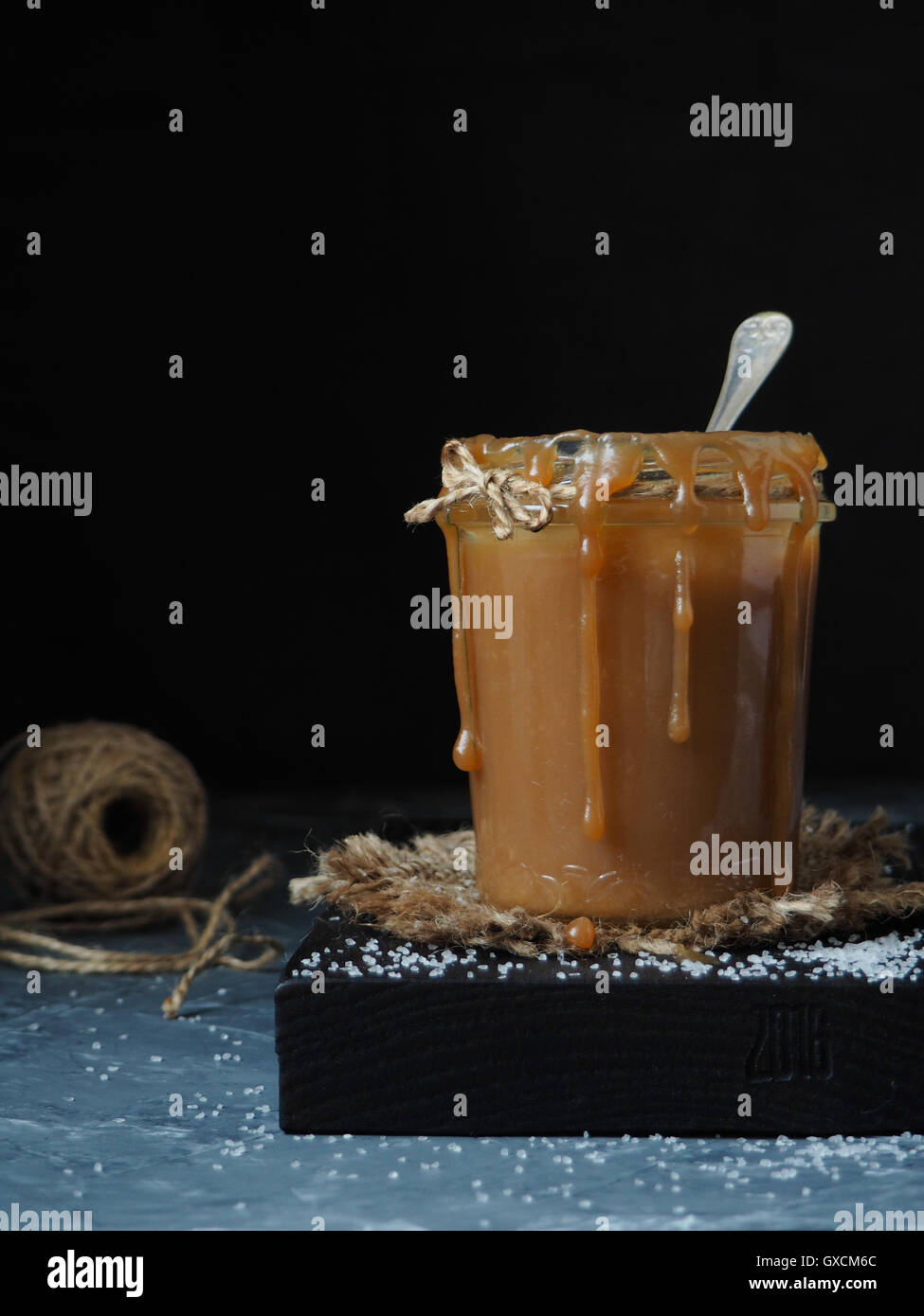 Sauce caramel salé fait maison rustique dans un bocal en verre, saupoudré de sel. Fond noir Banque D'Images