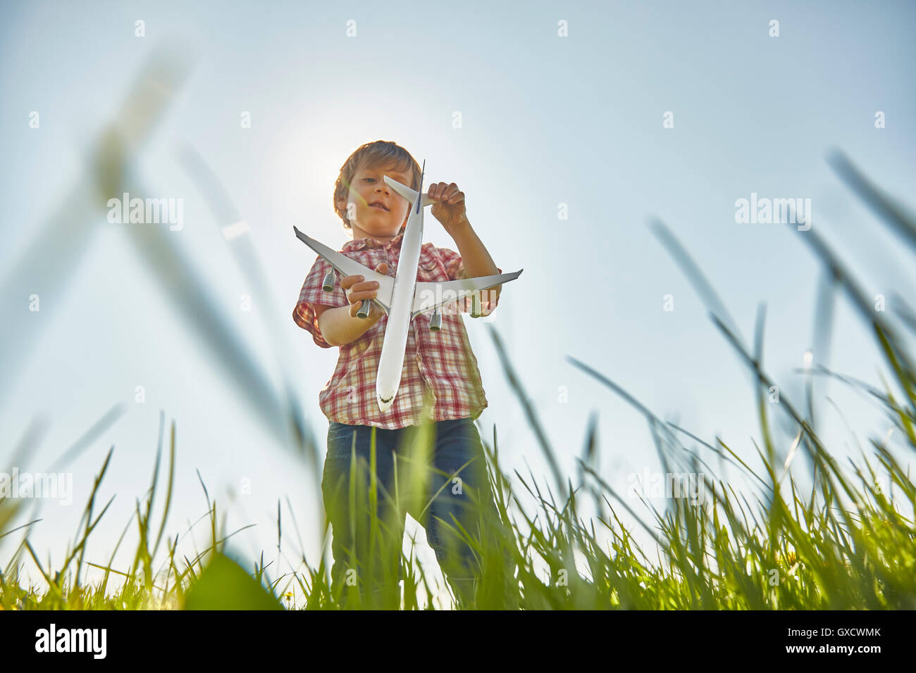 Low angle view of boy standing in grass contrôle de queue toy airplane Banque D'Images