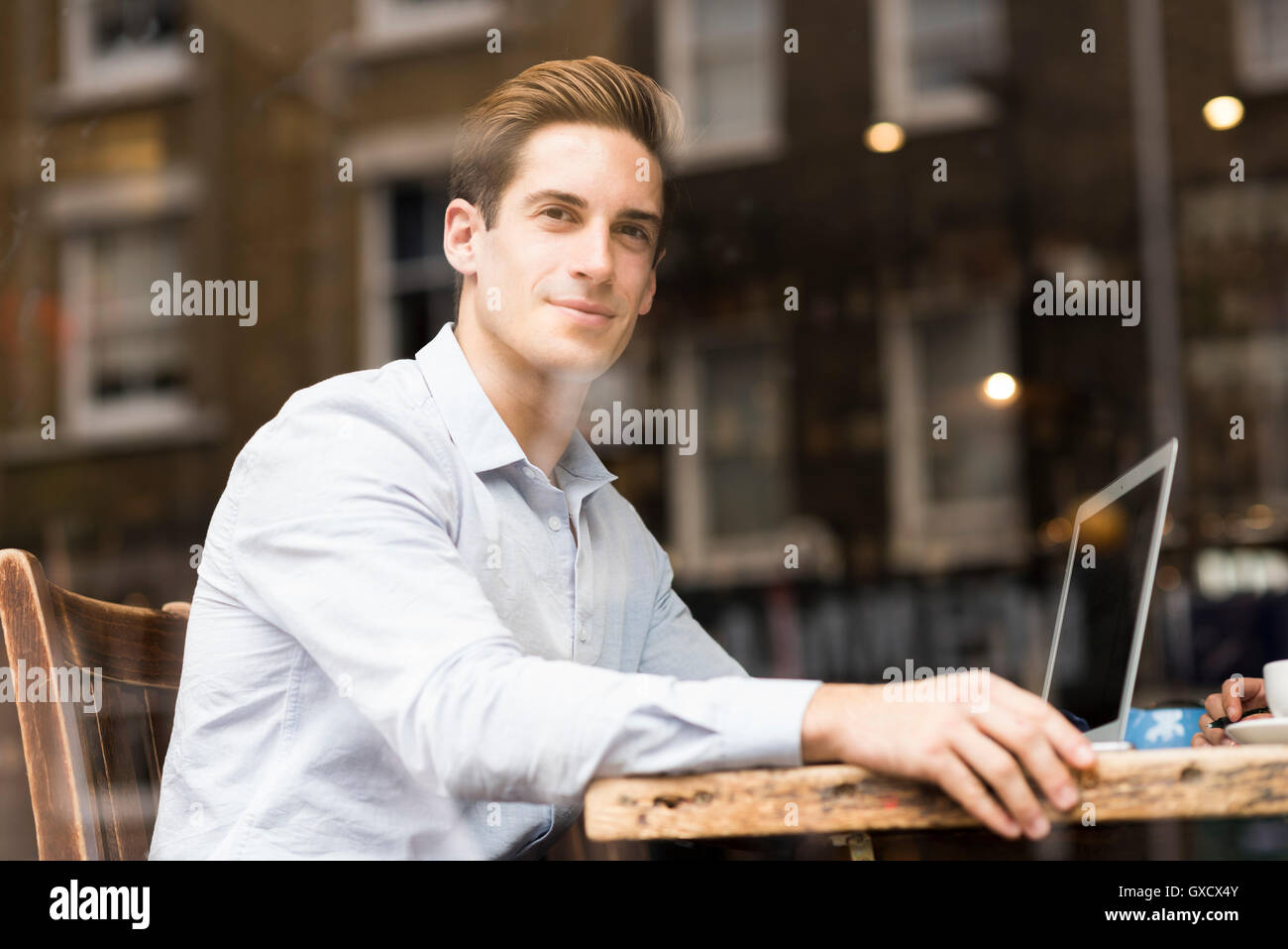 Window view of young businessman with laptop in cafe Banque D'Images