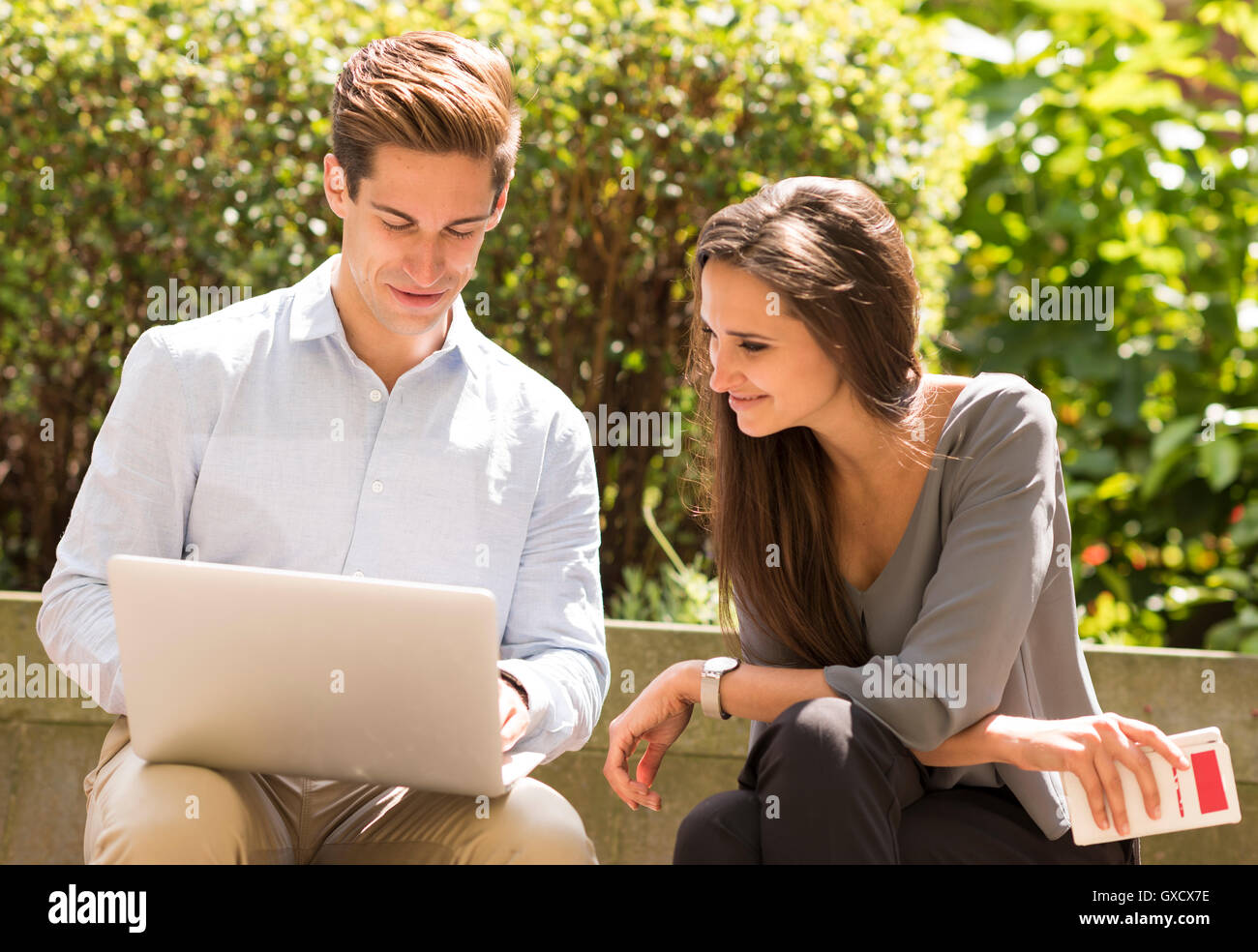 Businessman and woman reading laptop sur banc de parc, London, UK Banque D'Images