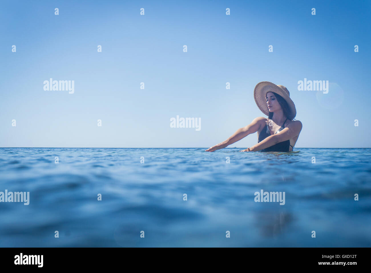 Young woman wearing sunhat patauger dans la mer d'un bleu profond, Villasimius, Sardaigne, Italie Banque D'Images