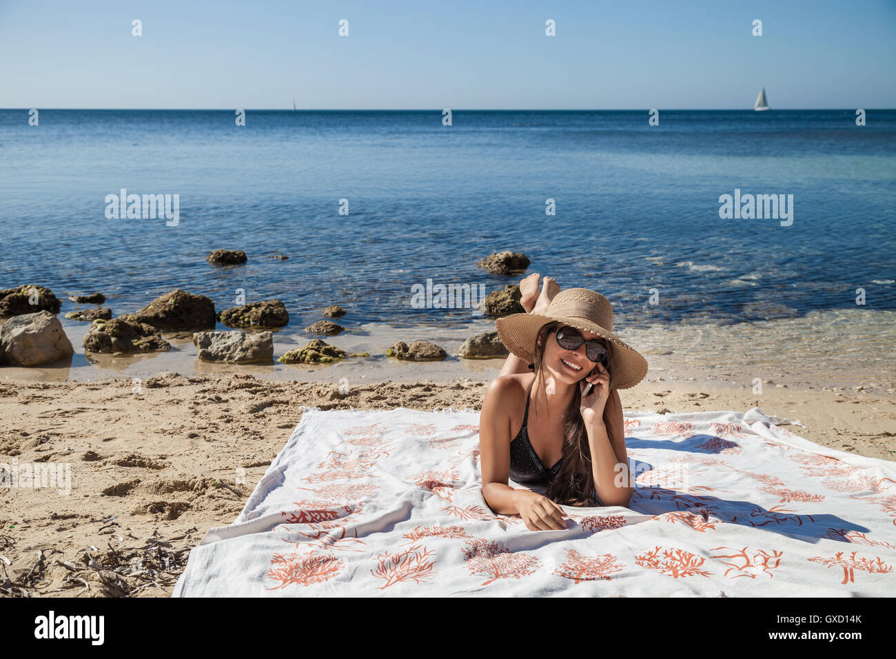 Young woman chatting on smartphone tout en bronzant sur la plage, Villasimius, Sardaigne, Italie Banque D'Images