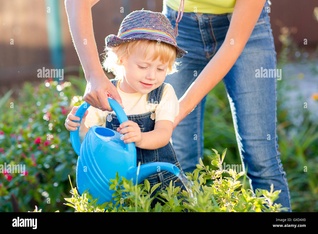 Tout-petit enfant mère aidant dans le jardin d'été ensoleillé Banque D'Images