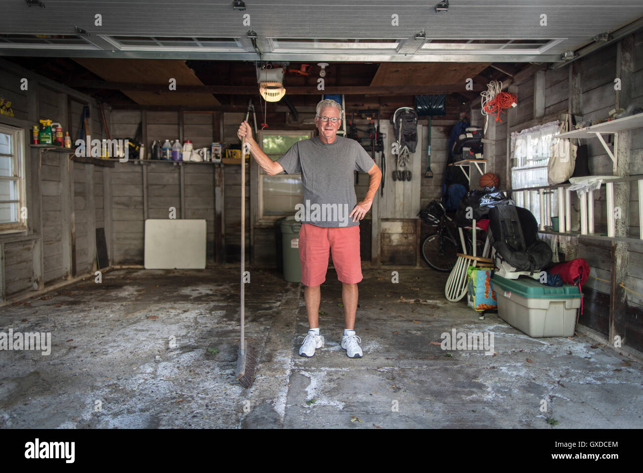 Portrait of senior man standing in garage holding broom Banque D'Images