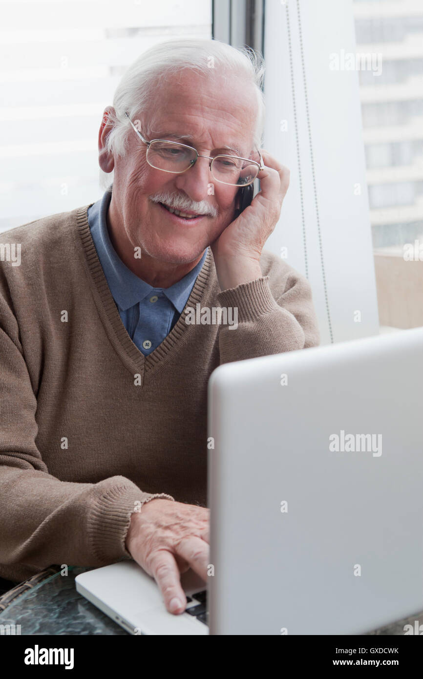 Senior man using mobile phone and laptop at home Banque D'Images