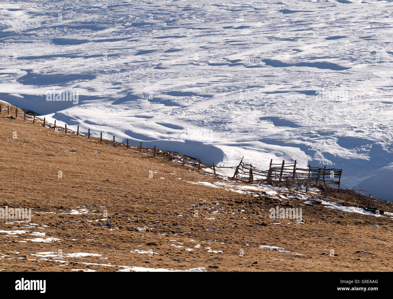 Le rural clôture en bois sur la colline pente partiellement couvert par la neige par une belle journée d'hiver. Peut être utilisé comme arrière-plan, papier peint Banque D'Images