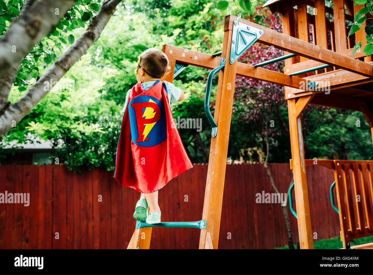 Young boy wearing superhero costume grimpant sur une aire d'arrière-cour Banque D'Images