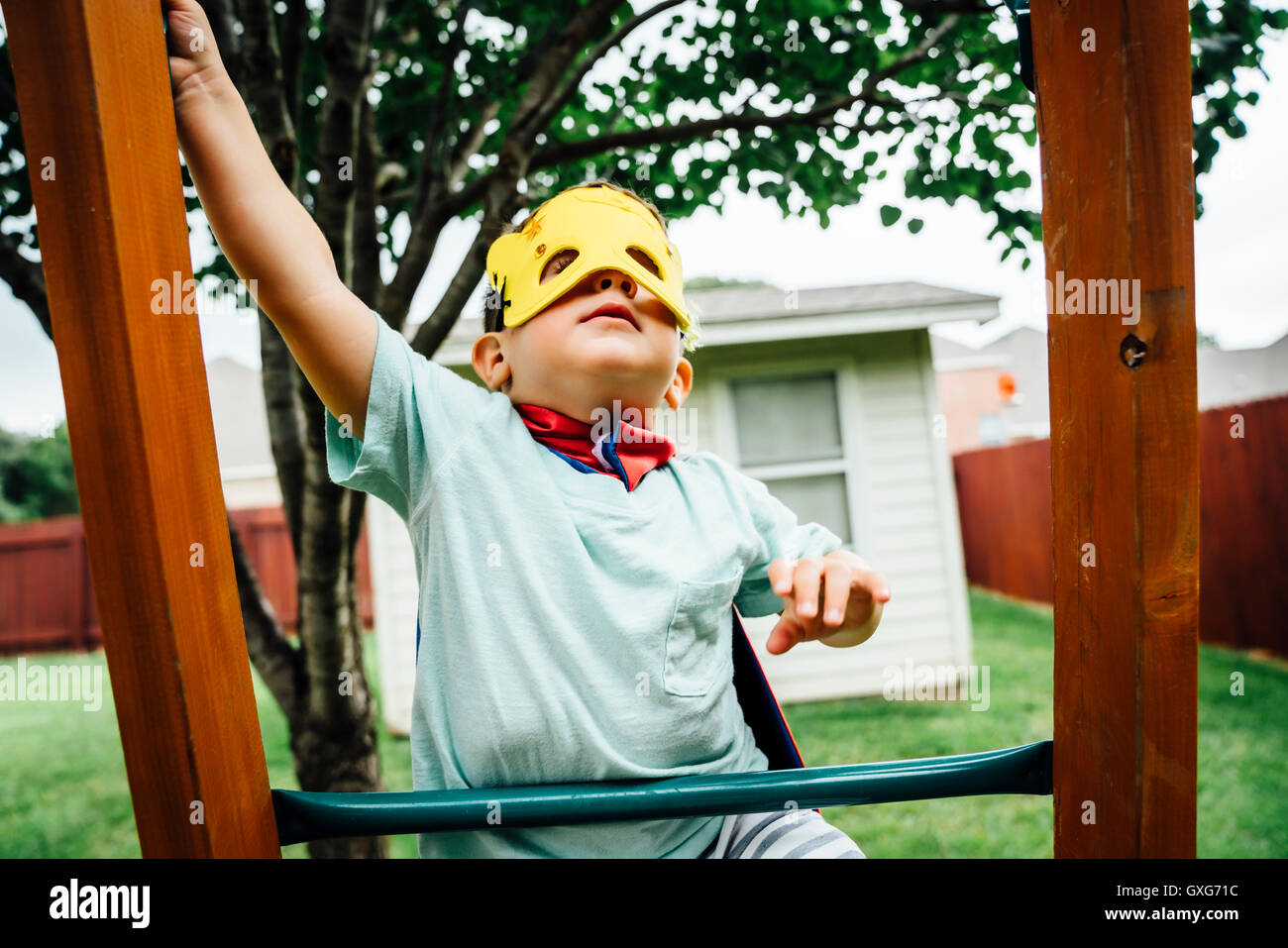 Young boy wearing superhero costume grimpant sur une aire d'arrière-cour Banque D'Images