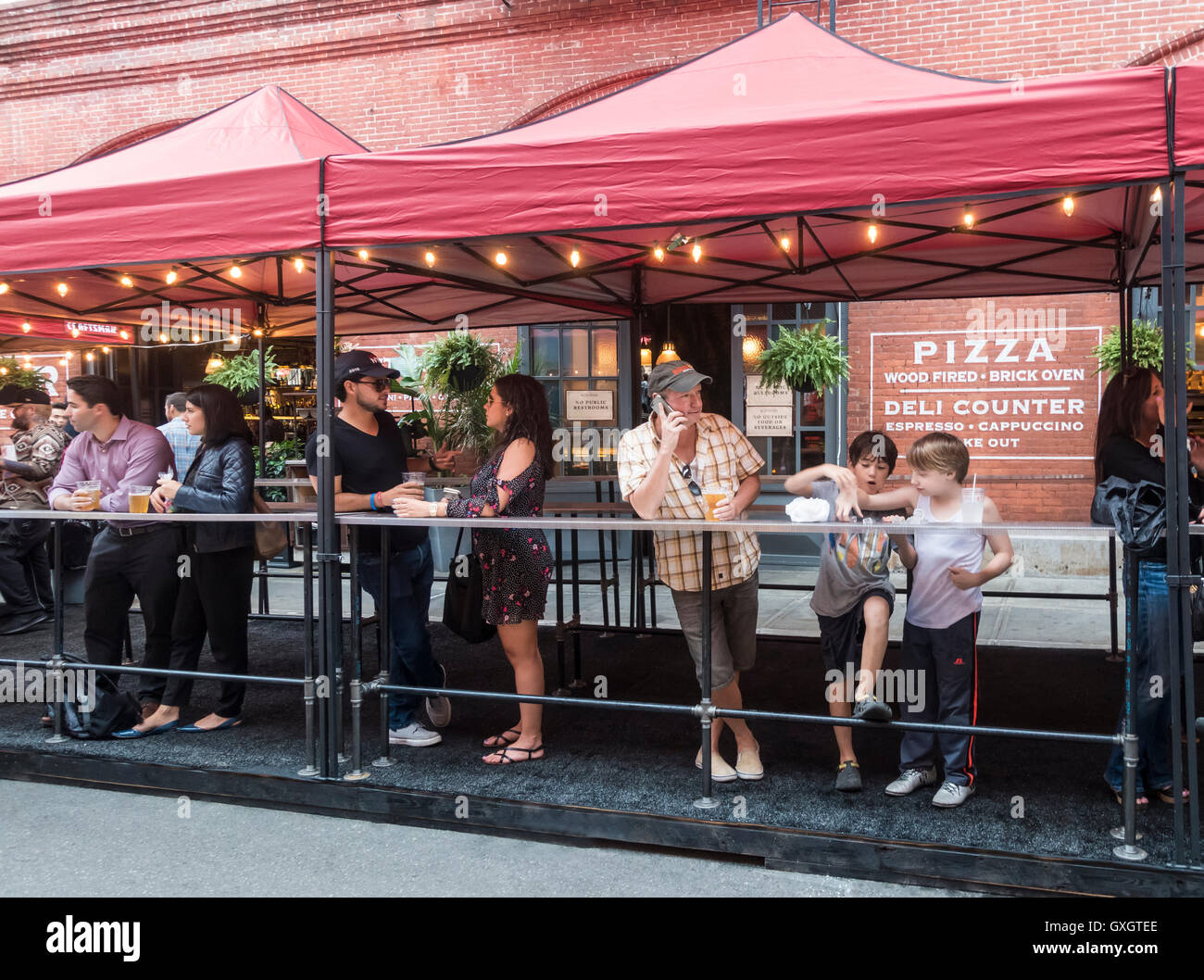 Les adultes se détendre avec une bière tandis que les garçons imbécile autour à un stand de rue sur Mulberry Street pendant la fête de San Gennaro dans Little Italy, New York City Banque D'Images