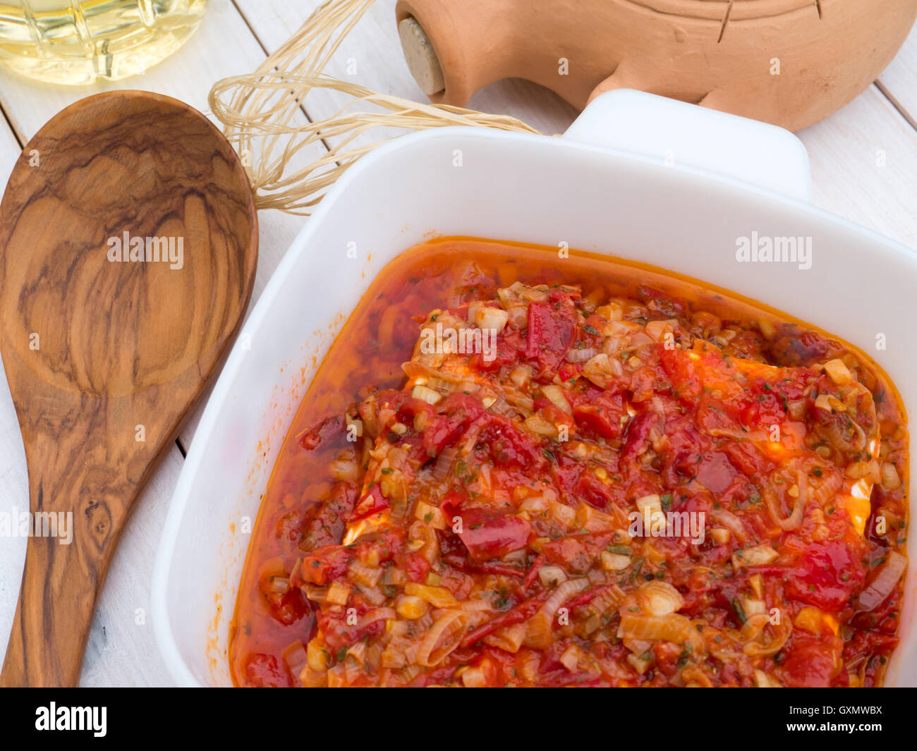 Feta grecque au four avec tomates, oignon, ail, huile d'olive et les herbes dans le bol blanc sur la table en bois blanc Banque D'Images