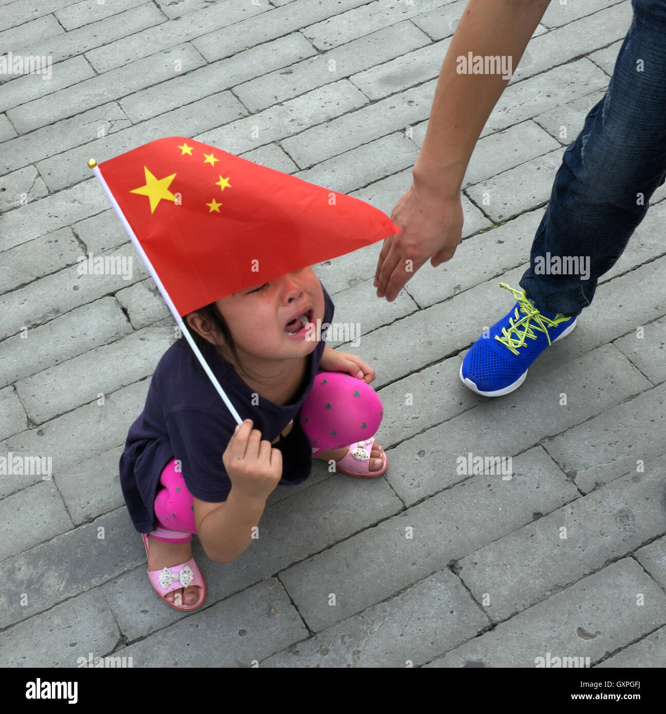 Une petite fille chinoise en pleurs, avec un drapeau national tout en visitant la cité interdite à Pékin, en Chine. Banque D'Images