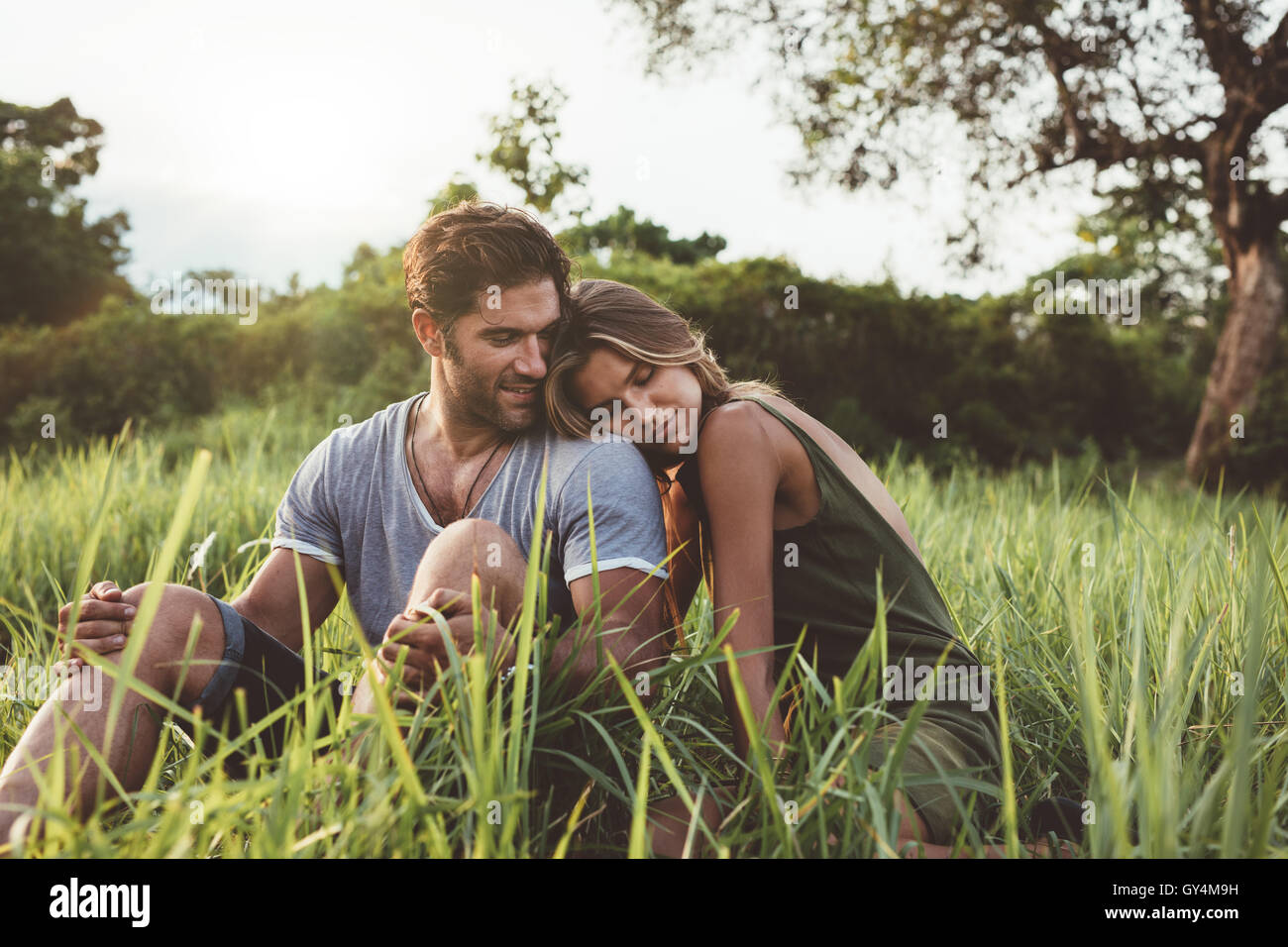 Shot de young couple sitting in meadow. L'homme et de la femme se détendre ensemble dans le domaine de l'herbe dans la campagne. Banque D'Images