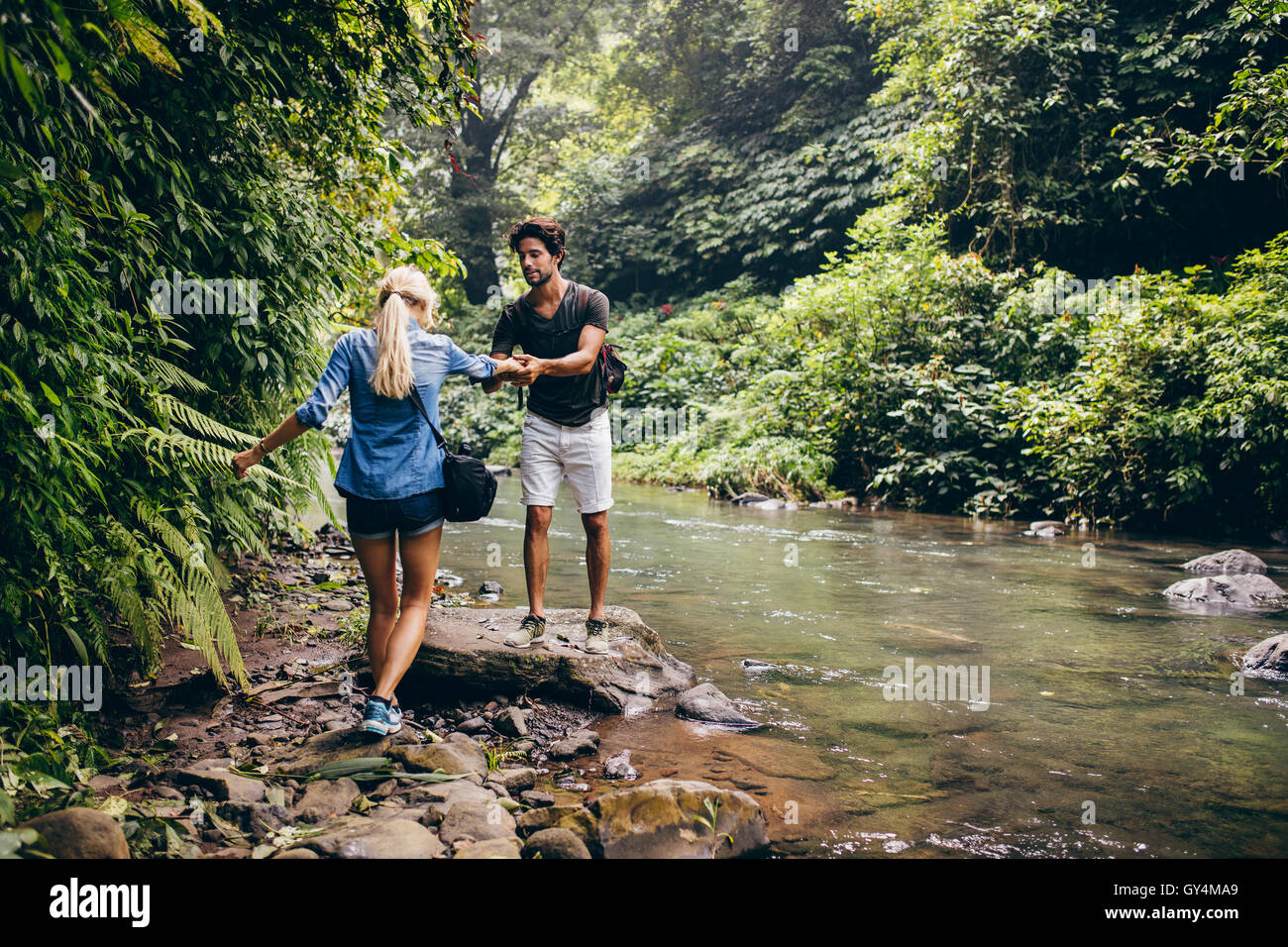 Couple dans la forêt par le flux. Jeune couple en train de marcher sur les rochers par le ruisseau de montagne avec l'homme d'aider son amie. Banque D'Images