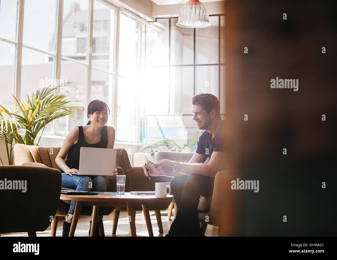 Shot de businessman sitting in office lobby talking and smiling. Woman with laptop discuter affaires idées avec leurs collègues masculins Banque D'Images