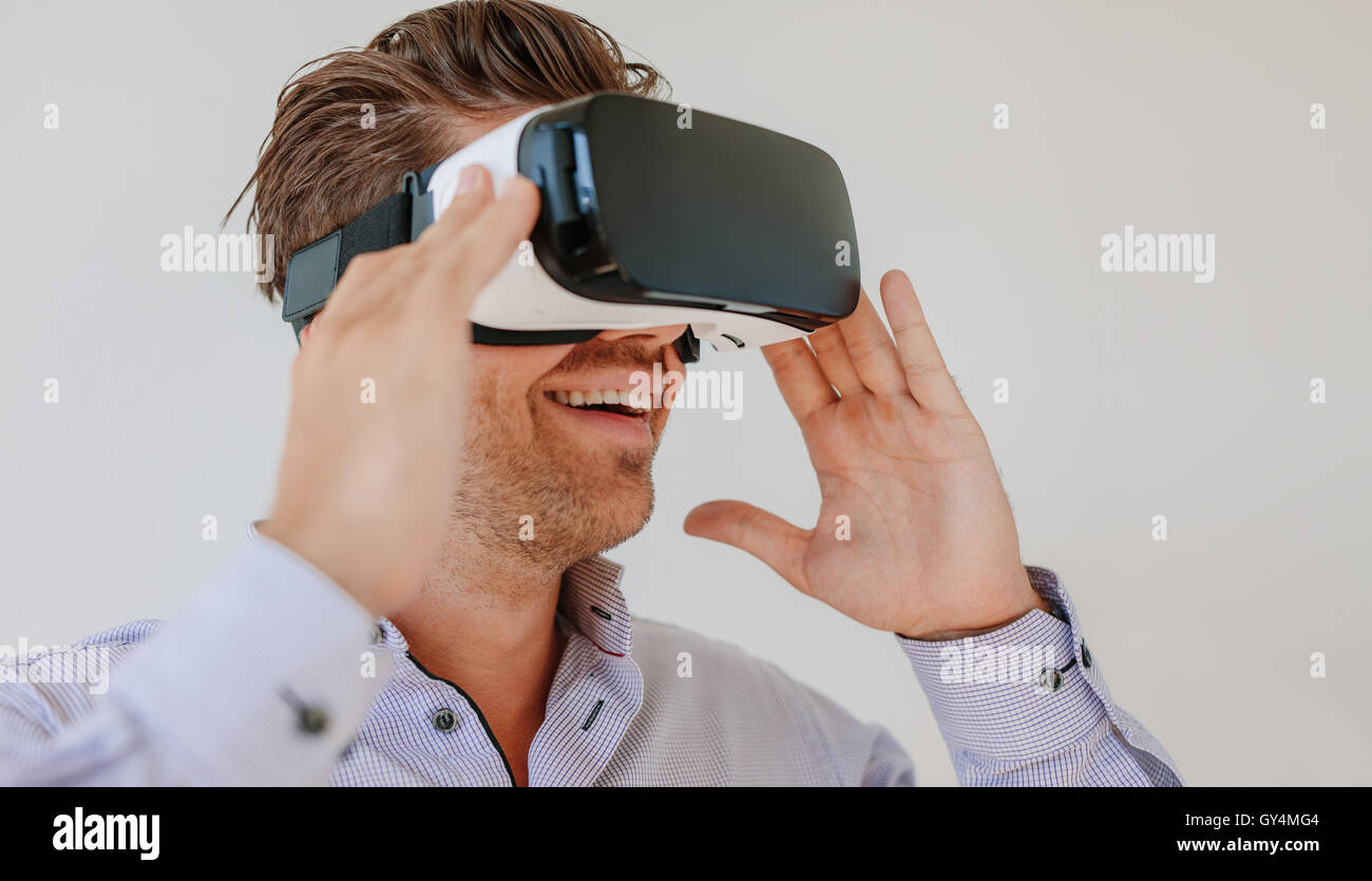 Photo de heureux jeune homme portant des lunettes de réalité virtuelle contre un arrière-plan gris. Homme de race blanche à l'aide de lunettes VR et souriant. Banque D'Images
