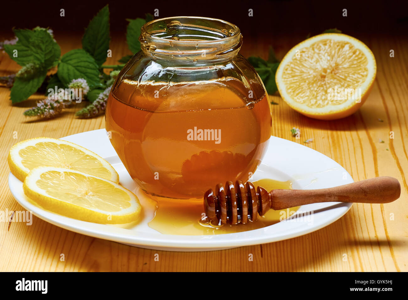 Pot de miel sur plaque blanche avec goutteur, tranches de citron et menthe floraison Banque D'Images