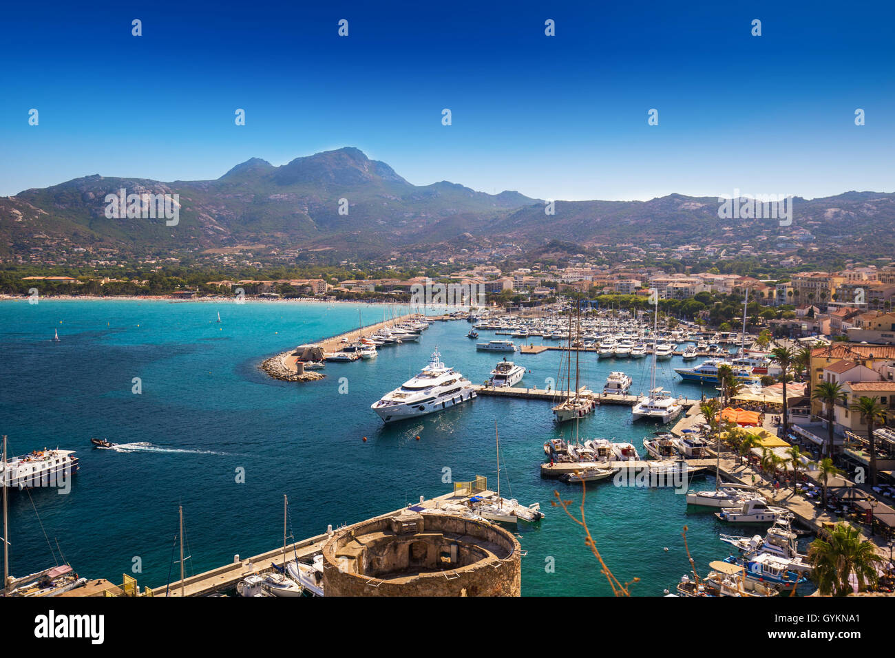 Vue de la plage de Calvi, les maisons historiques de la vieille ville de Calvi avec de l'eau dans l'océan turquoise clair port avec bateaux et yachts, Corse Banque D'Images
