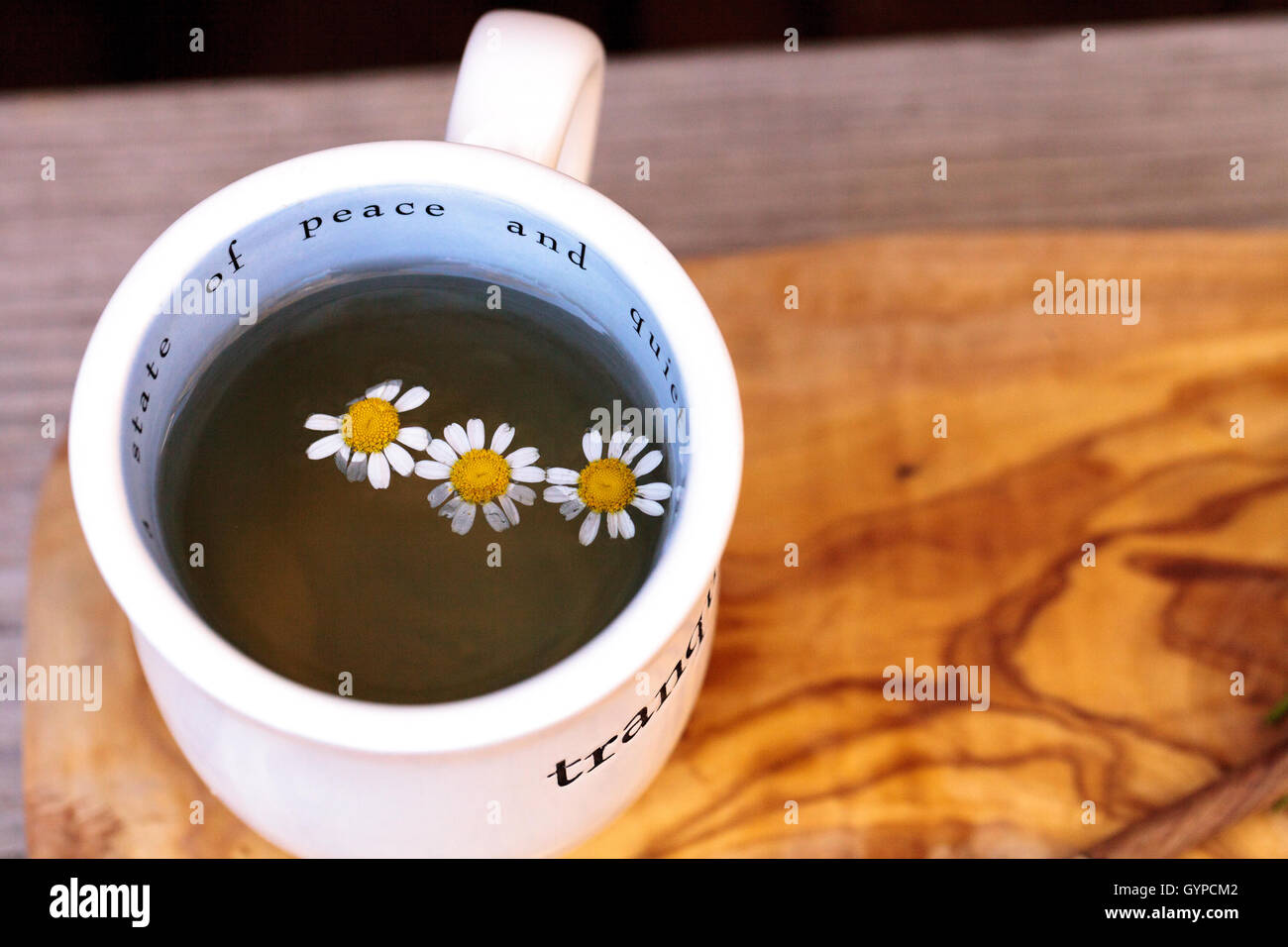 Avec la Camomille Camomille fleurs daisy blanc chaud dans une tasse sur une planche à découper et le rustique en bois, d'une cuillère. Ce remède à la maison est Banque D'Images