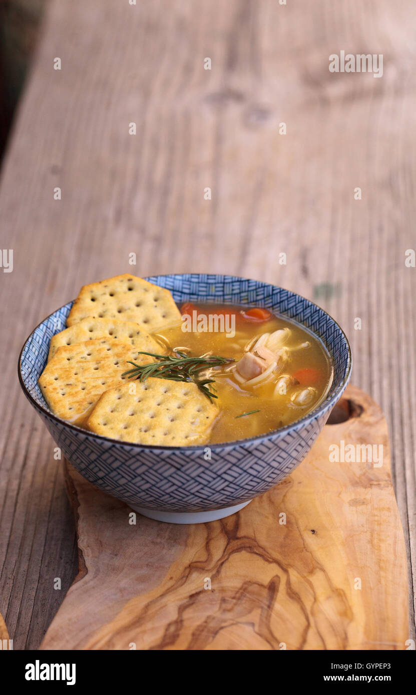 Soupe au poulet et nouilles dans un bol bleu et blanc avec des craquelins, tous assis sur une planche à découper en bois. Banque D'Images