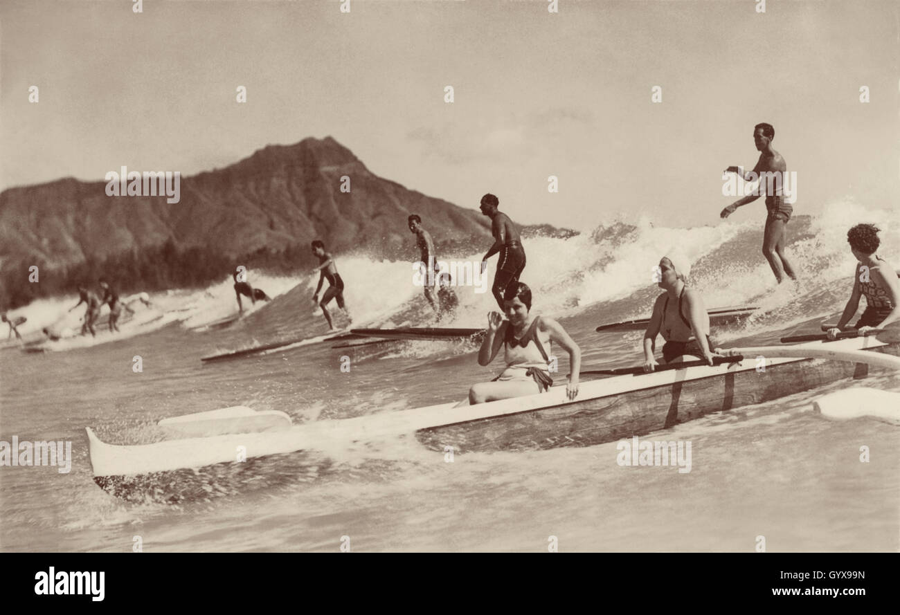 Vue sur les vagues de Waikiki, Honolulu, avec des hommes sur des planches de surf en bois et des femmes dans un bateau à outrigger. Photo de Tom Blake, 1931. Banque D'Images