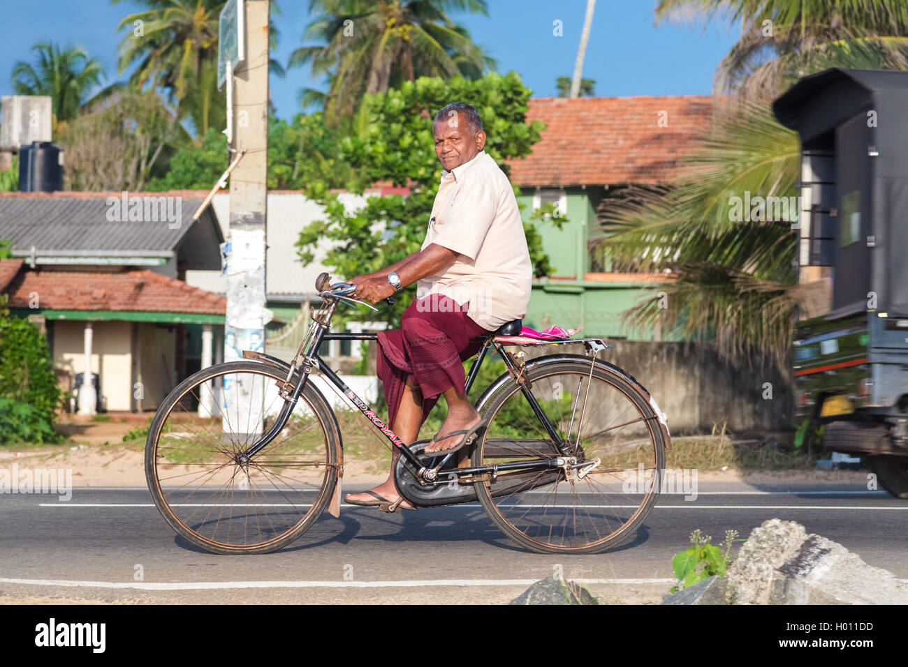 HIKKADUWA, SRI LANKA - le 24 février 2014 : un homme âgé en jupe et chemise  de rouler à vélo. Le vélo est le moyen de transport principal f Photo Stock  - Alamy