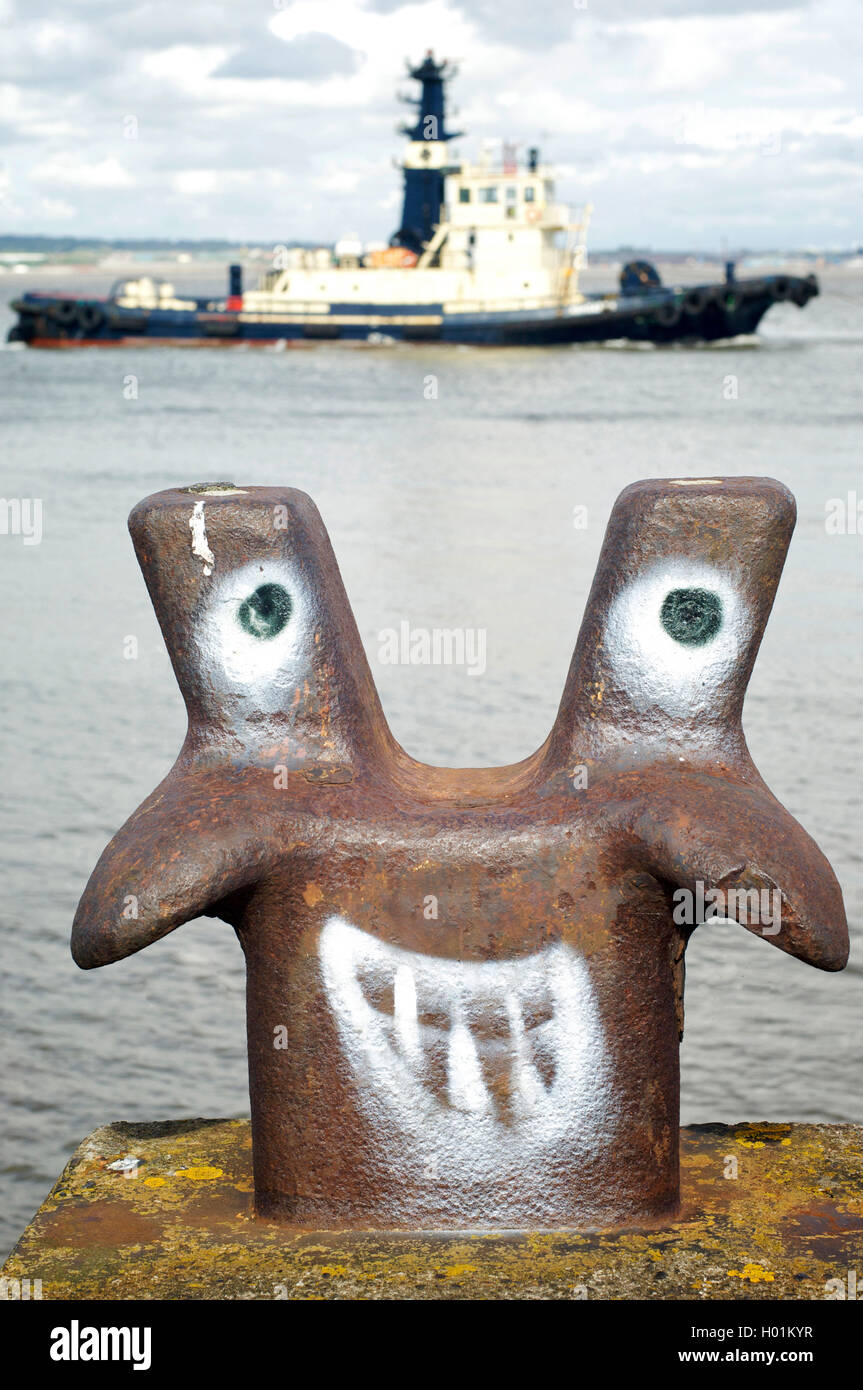 Drôle visage spray peint sur le bollard marin d'amarrage sur la rivière Mersey à Liverpool avec remorqueur passant en arrière-plan Banque D'Images
