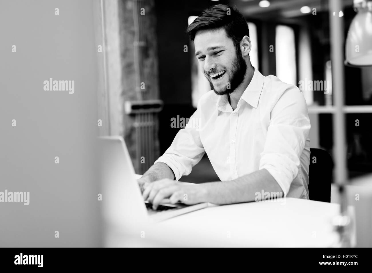 Beau mâle travailler dans un bureau et de la saisie sur un ordinateur portable tout en souriant Banque D'Images