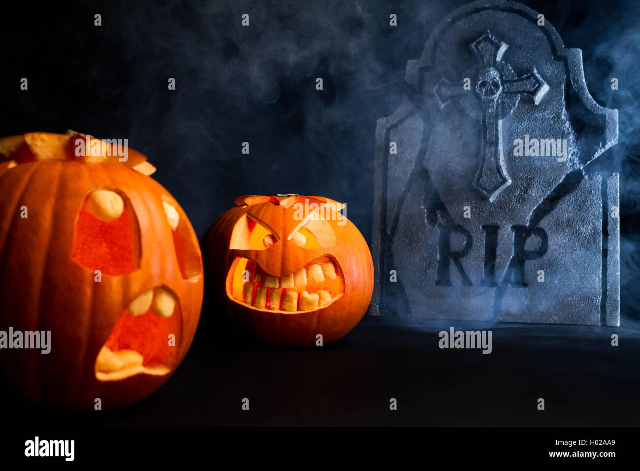 Peur et visage en colère face à des citrouilles d'halloween avec pierre tombale sur misty fond sombre. Banque D'Images