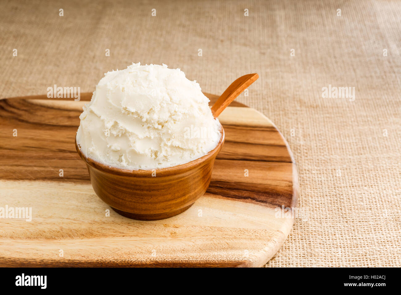 Beurre de karité bio non raffinée, dans le bol en bois avec la cuillère, se tient sur la planche de bois, tissu jute d'arrière-plan. Banque D'Images