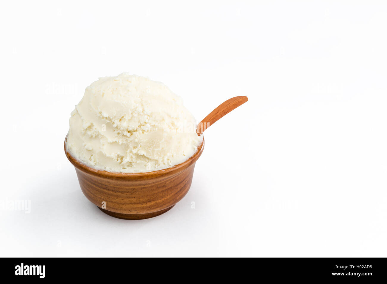 Beurre de karité bio non raffinée, dans le bol en bois avec la cuillère, debout sur le fond blanc pur. Banque D'Images