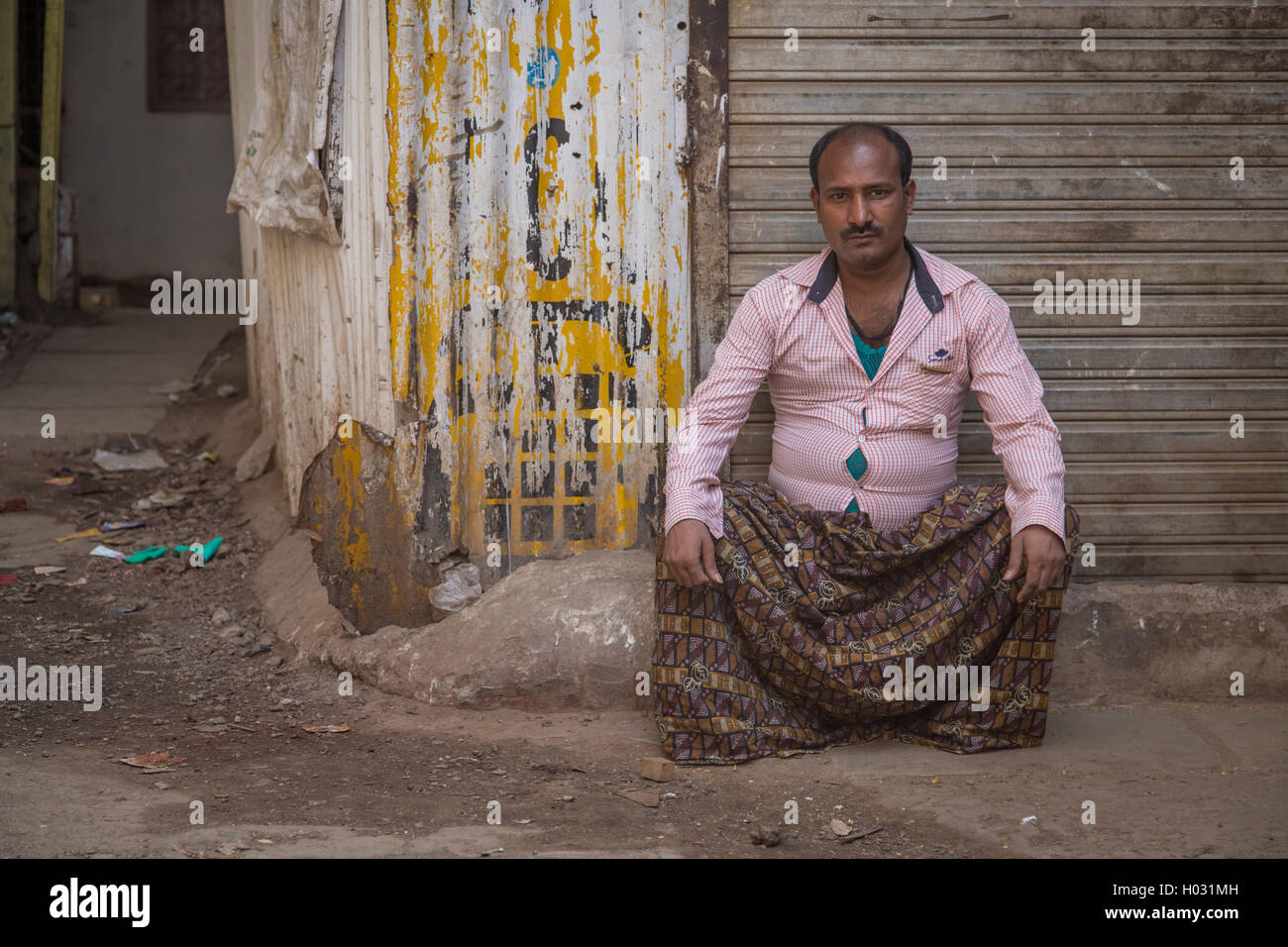 MUMBAI, INDE - 12 janvier 2015 : Indian man avec moustache est assis à côté de magasin fermé dans la rue vide sale dans brown lun à motifs Banque D'Images