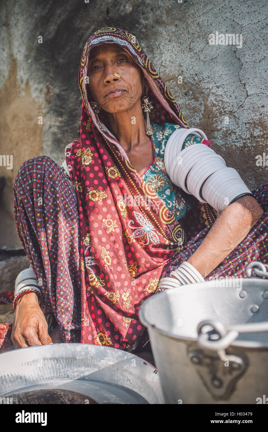 Région GODWAR, INDE - 13 février 2015 : Rabari tribeswoman en sari traditionnel décoré avec des bracelets de bras supérieur nettoie la vaisselle Banque D'Images