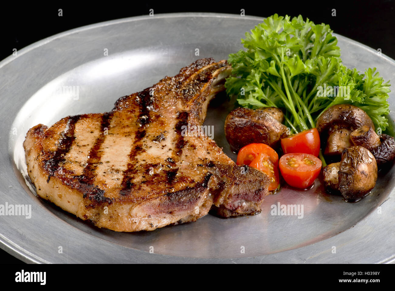 Côtelette de porc grillé aux champignons et tomates cerises. Banque D'Images