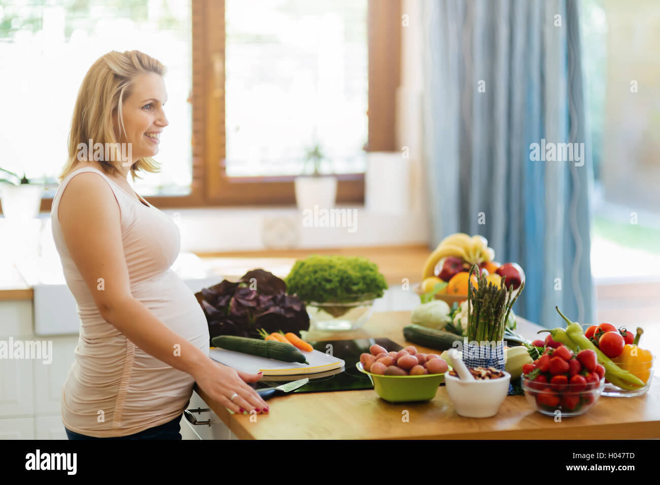 Belle femme enceinte, la préparation de repas sur l'île de cuisine à partir de produits frais Banque D'Images