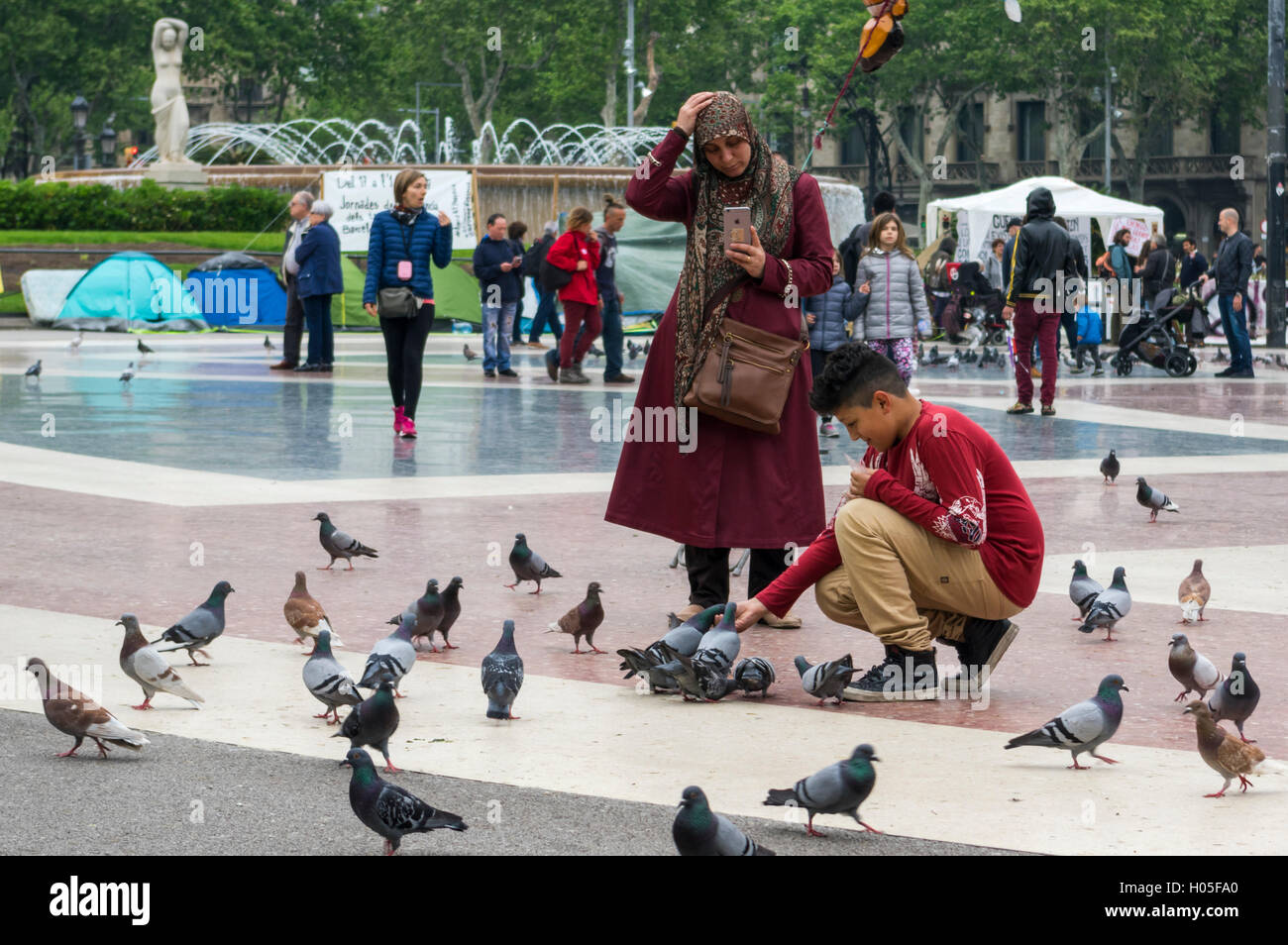 Garçon musulman nourrir les pigeons de la rue à Barcelone, tandis que le port du hijab-mère prend une photo de lui avec son iPhone. Banque D'Images