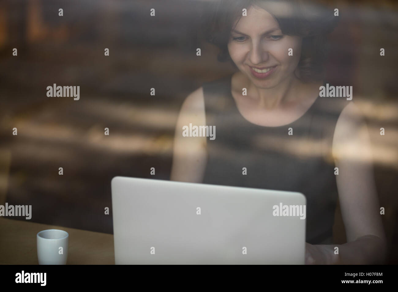 Portrait of happy smiling belle jeune femme assise dans le café moderne avec tasse de verre sur table, working on laptop Banque D'Images