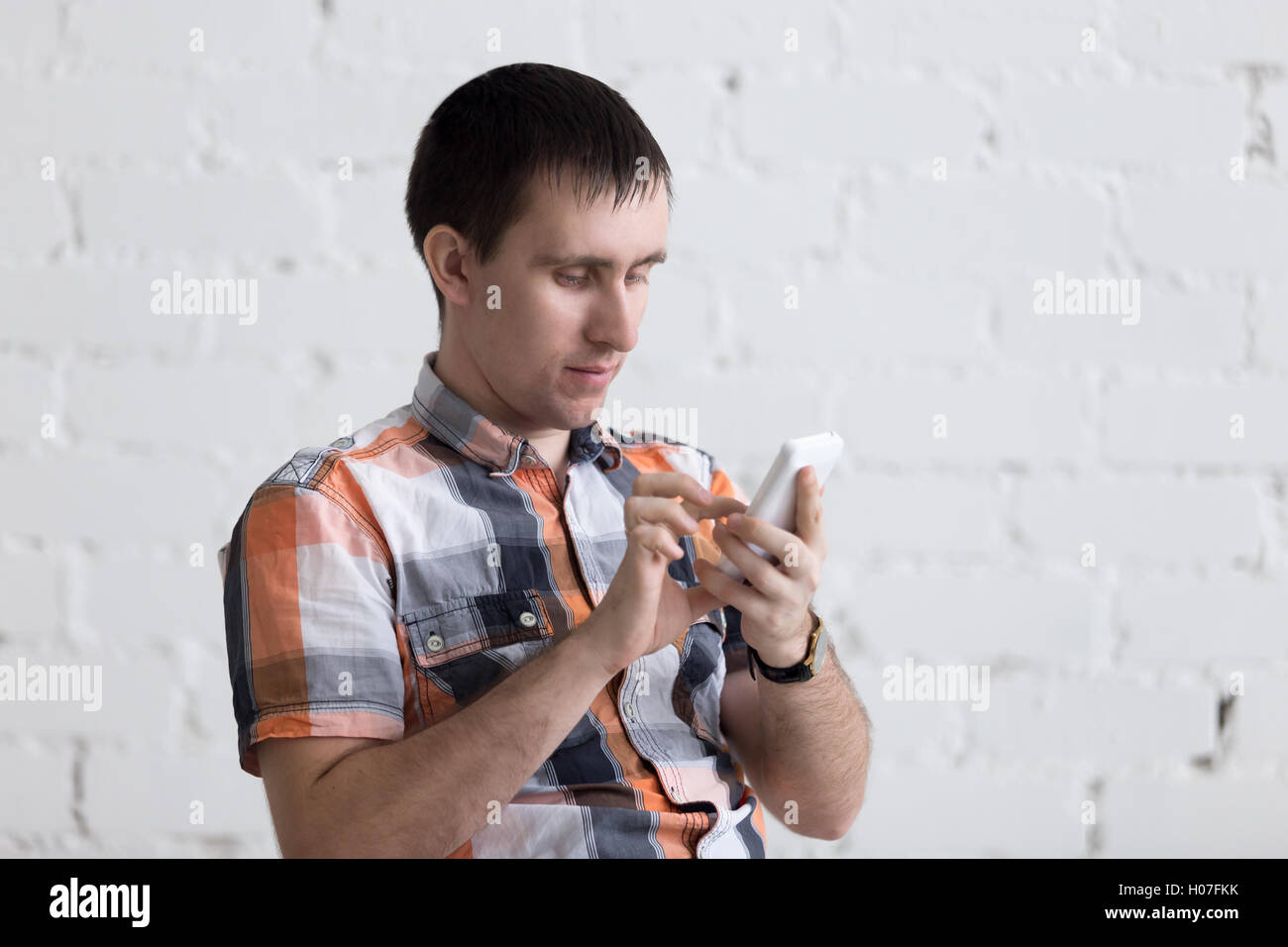 Portrait de casual young man holding mobile phone, à l'aide d'application pour smartphone, défilement, regardant l'écran, assis dans la salle avec Banque D'Images