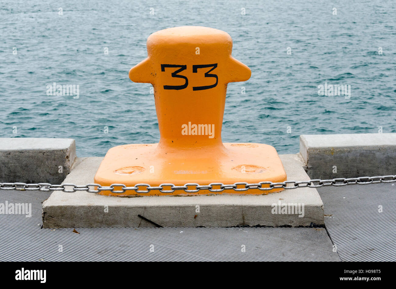 Amarrage jaune post, avec le numéro 33 peint sur en gris, sur la jetée à l'eau en arrière-plan et la chaîne en premier plan. Banque D'Images