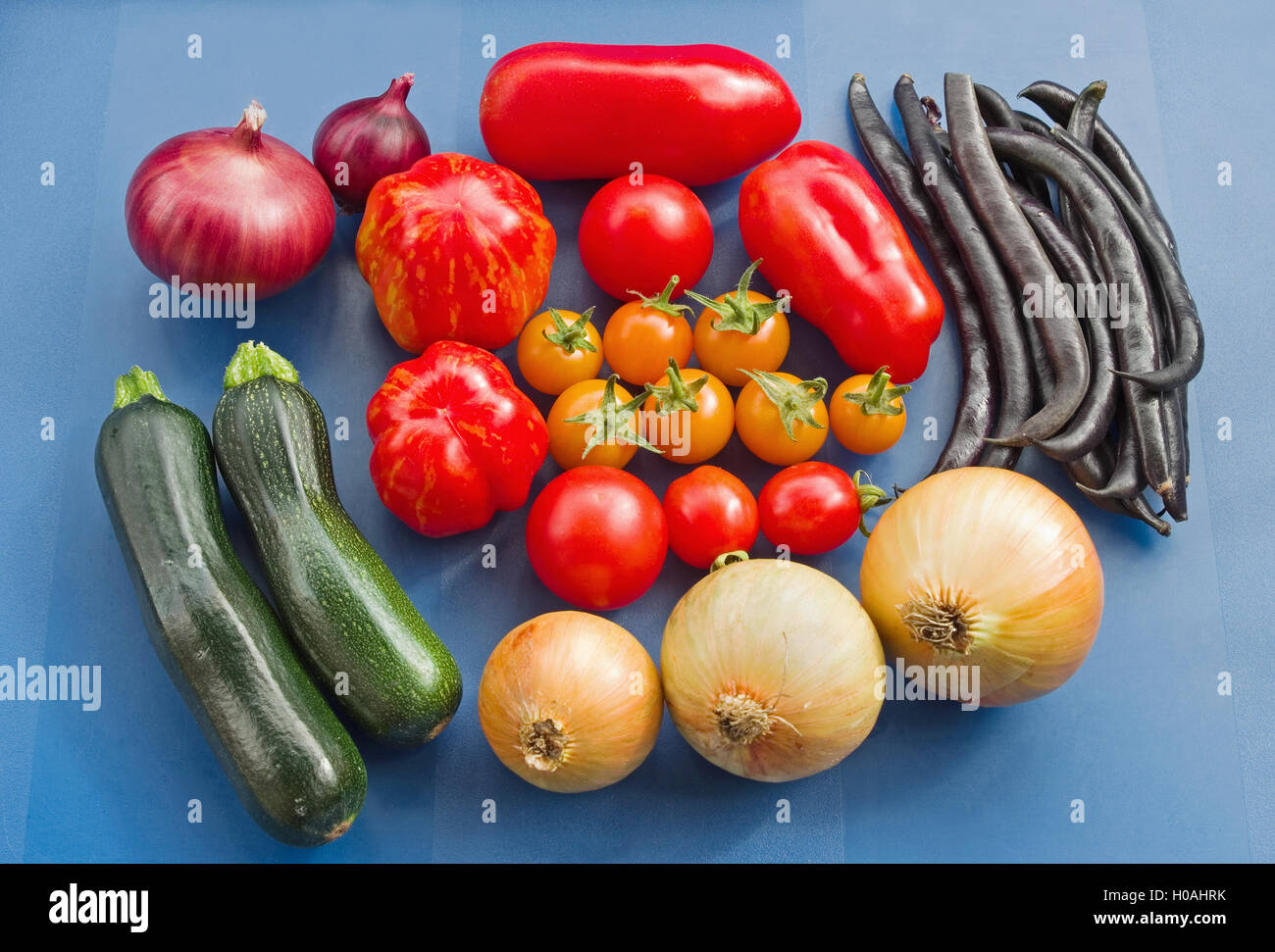 Arrangement d'un assortiment de variétés de tomates fraîchement cueillies, et autres légumes du jardin d'été, sur un fond bleu. Banque D'Images